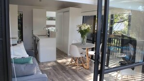 A modern living space with a sofa, a dining table with chairs, a kitchen area, and a balcony with a glass door.