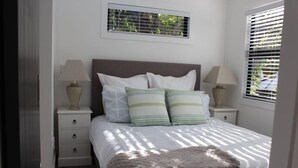 A neatly made bed with white bedding and striped pillows, flanked by two bedside tables with lamps.