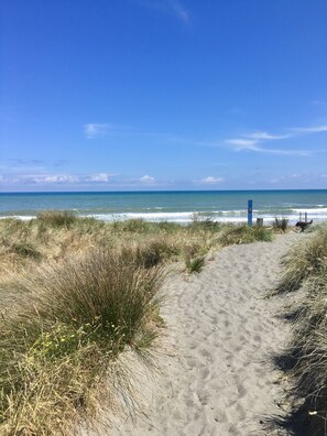 Ein sandiger Küstenpfad führt zum Meer, in der Ferne ein blaues Schild.