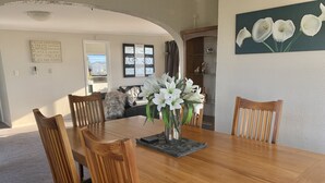 A dining area with a wooden table, chairs, and a vase of white flowers. - Seaviews, mountain views and sunsets (Otaki Beach)