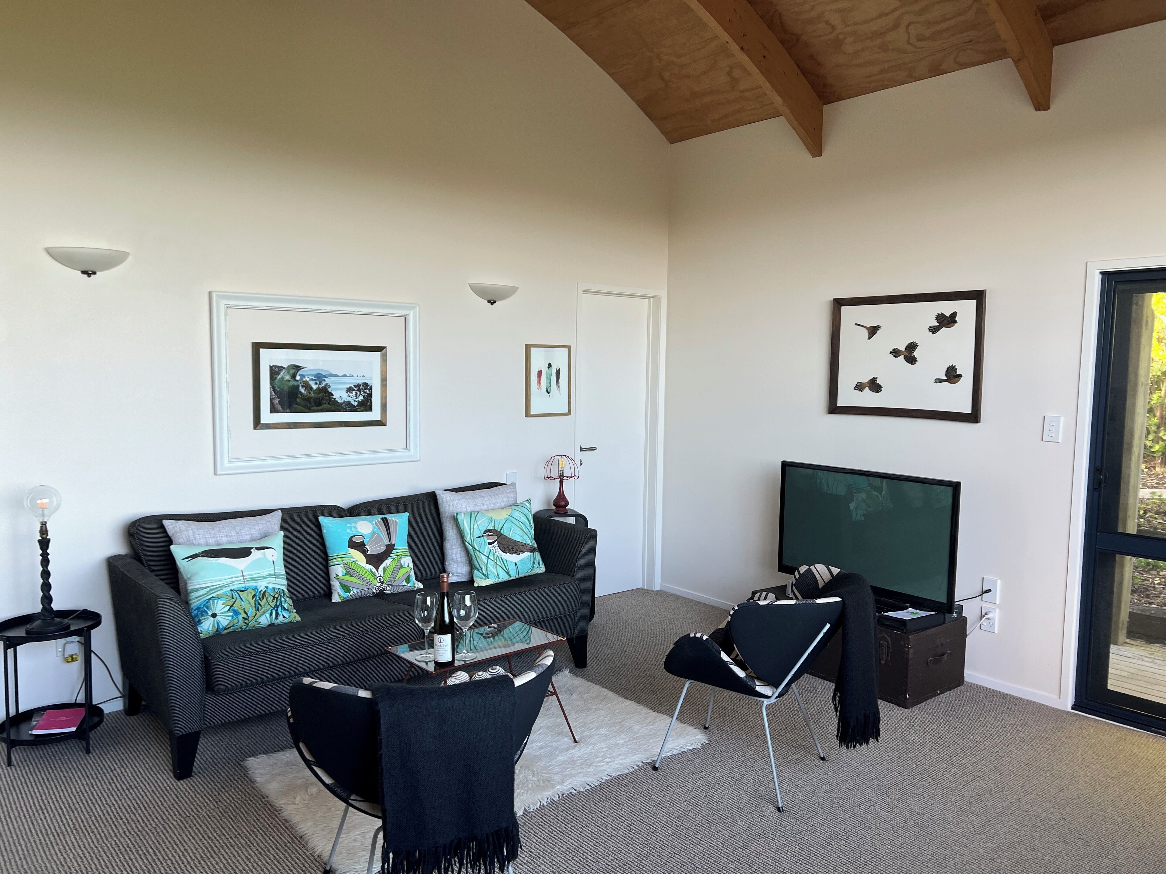A living room with a dark sofa, a glass coffee table, a TV, and framed pictures on the wall.