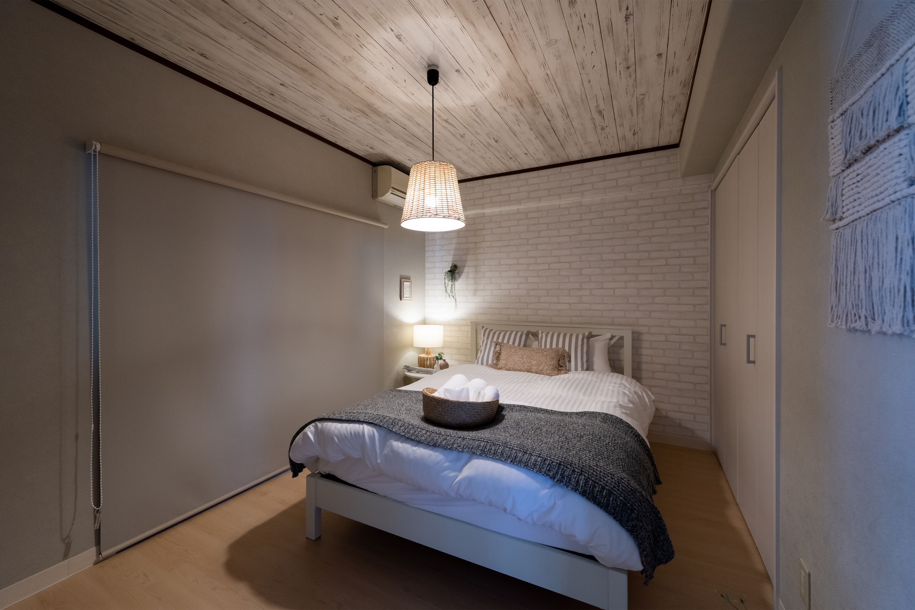 A bedroom with a white bed, a hanging light fixture, and a brick wall.