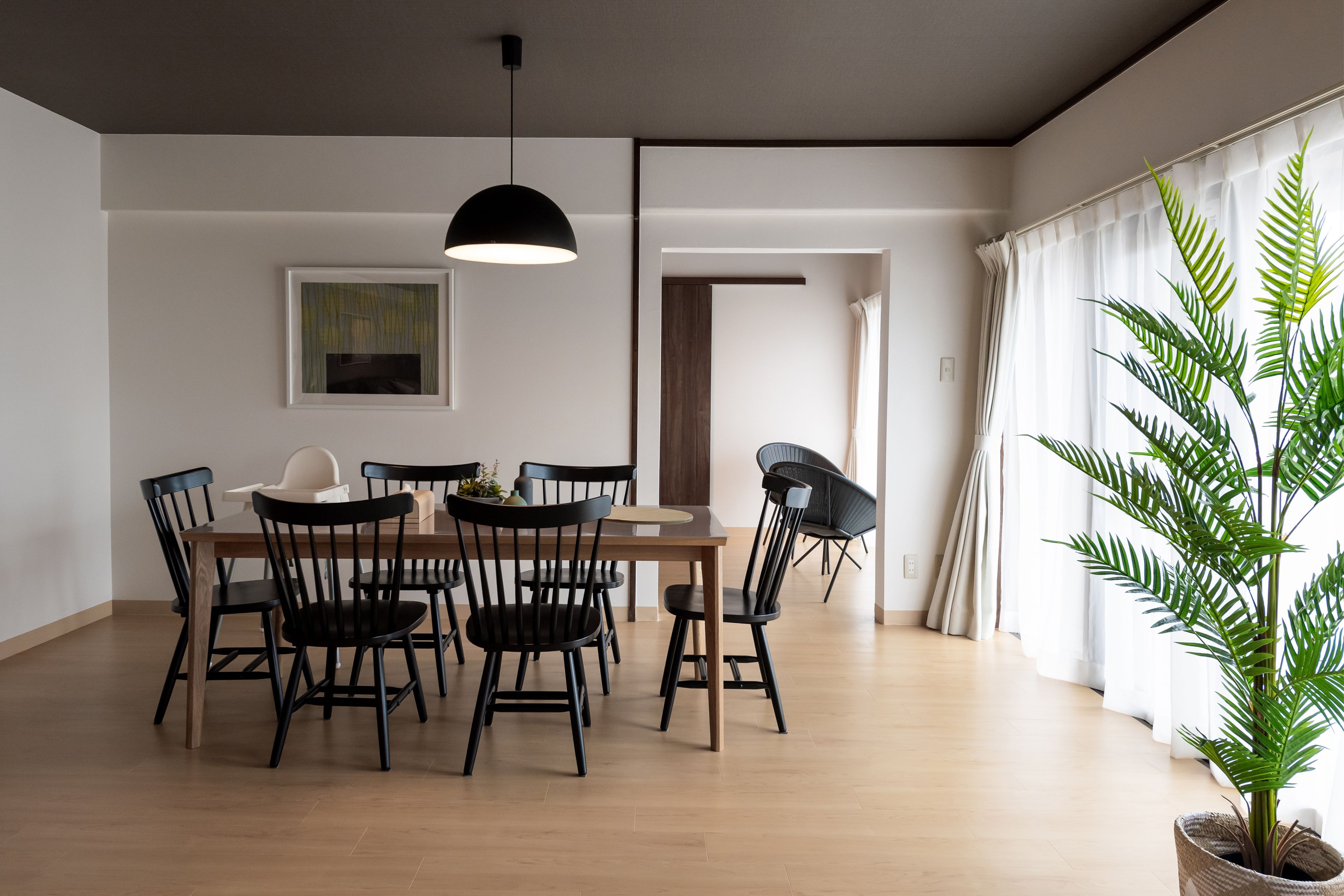 A dining area with a wooden table and black chairs, a pendant light, and a potted plant.