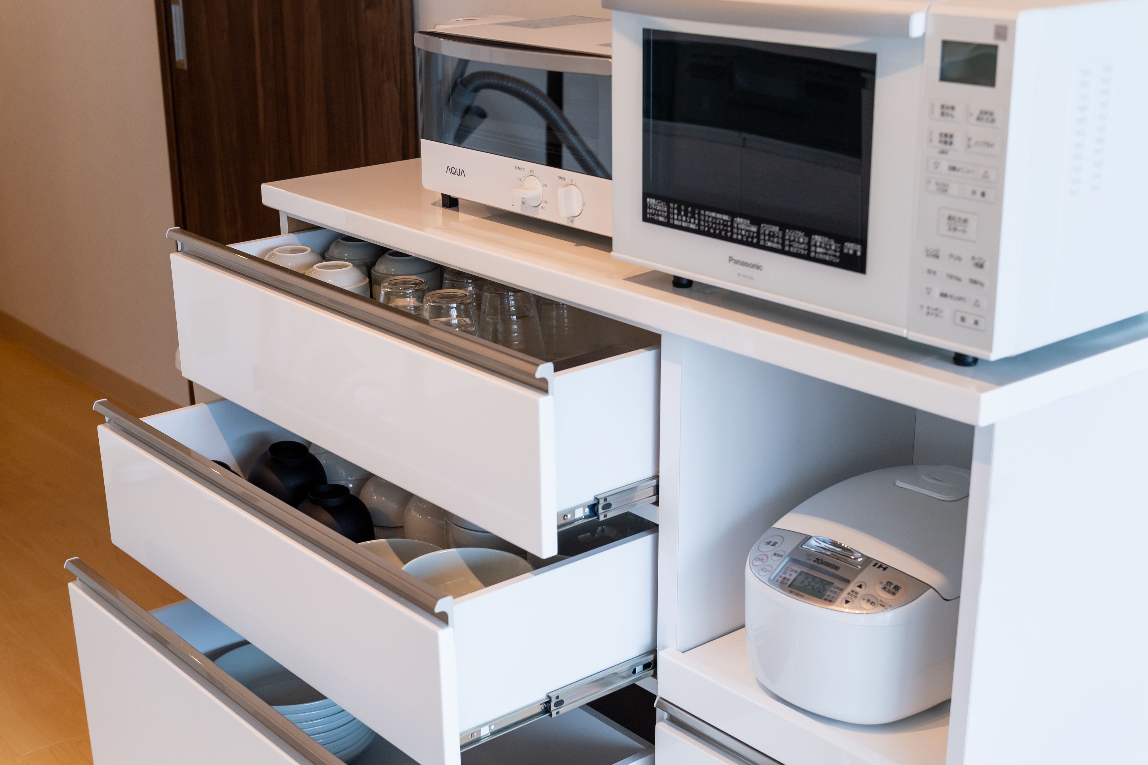 Una cucina con un forno a microonde, una cuociriso e un cassetto contenente utensili.