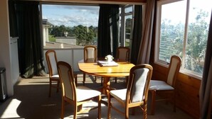Un coin repas avec une table ronde en bois et six chaises, de grandes fenêtres avec des rideaux et un ventilateur de plafond.