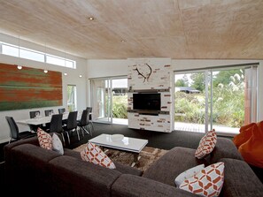 A modern living room with a fireplace, dining area, and large windows. - Stargazer - Ohakune Holiday Home (Ohakune)