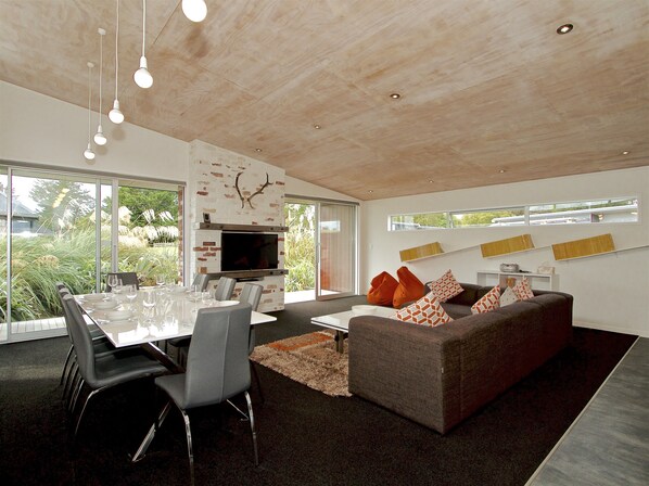 A modern living space with a dining area, a fireplace, and a sofa with patterned cushions. - Stargazer - Ohakune Holiday Home (Ohakune)