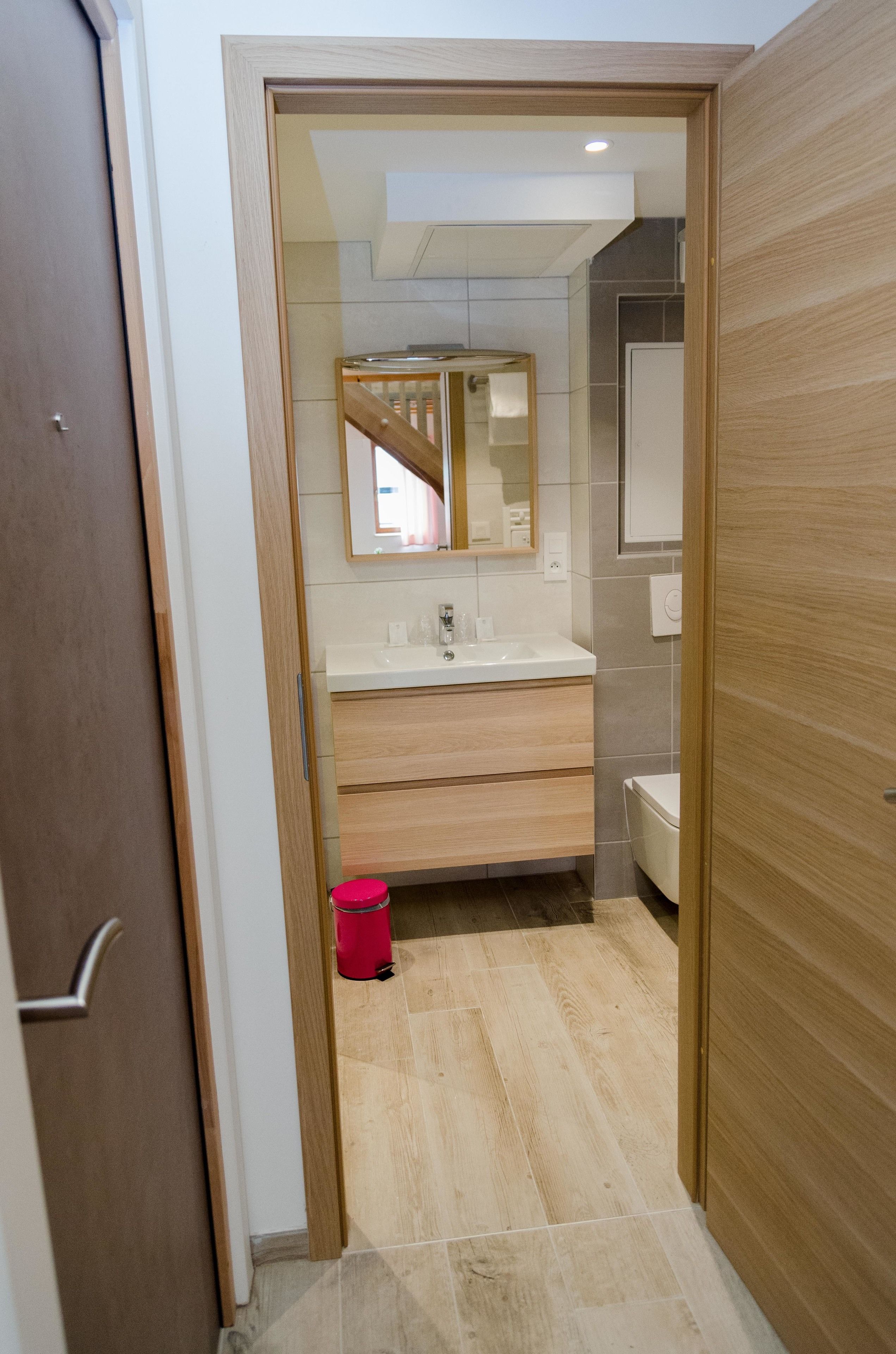 A modern bathroom with a wooden vanity, a mirror, and a toilet.