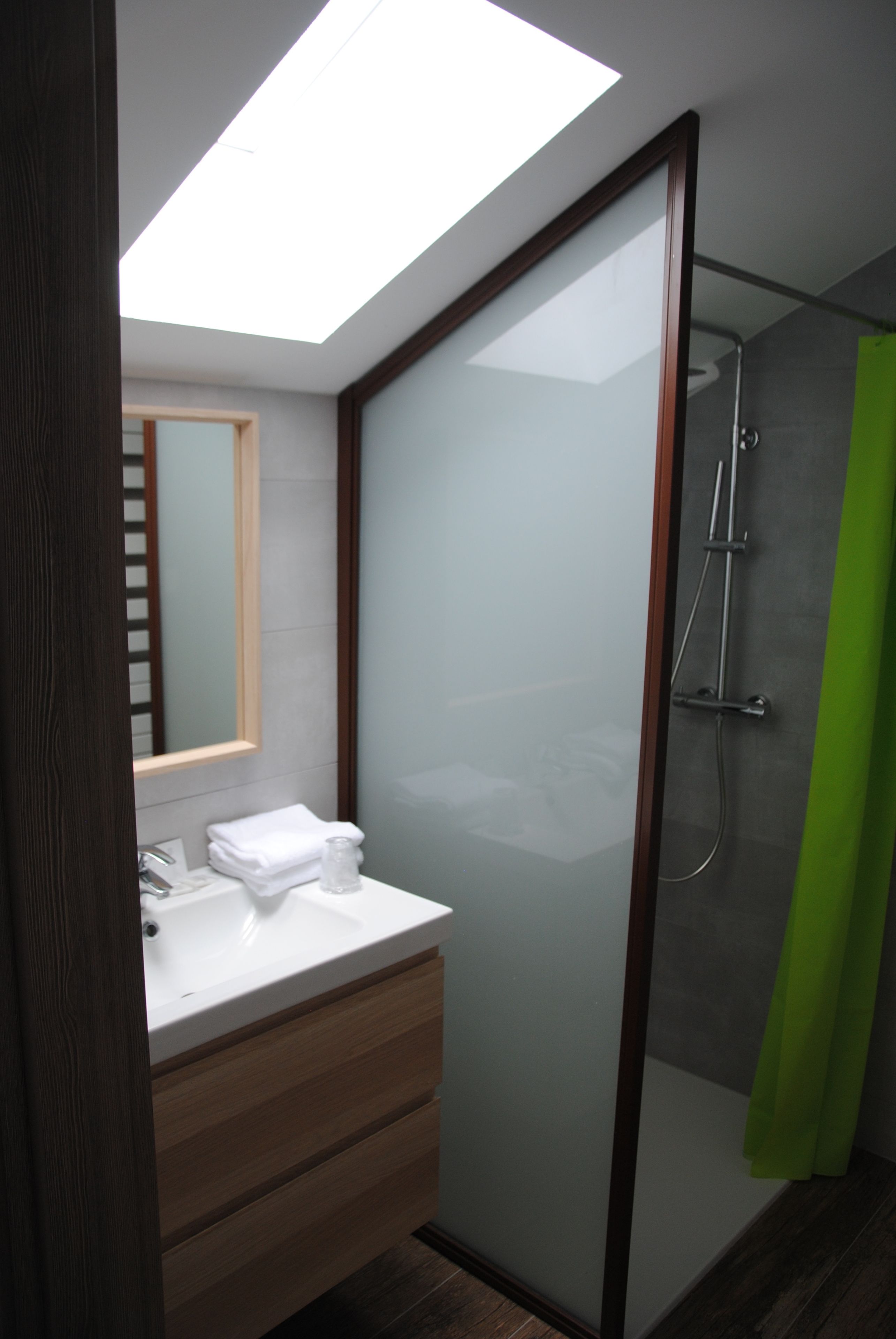 A modern bathroom with a skylight, a glass shower enclosure, and a wooden vanity.