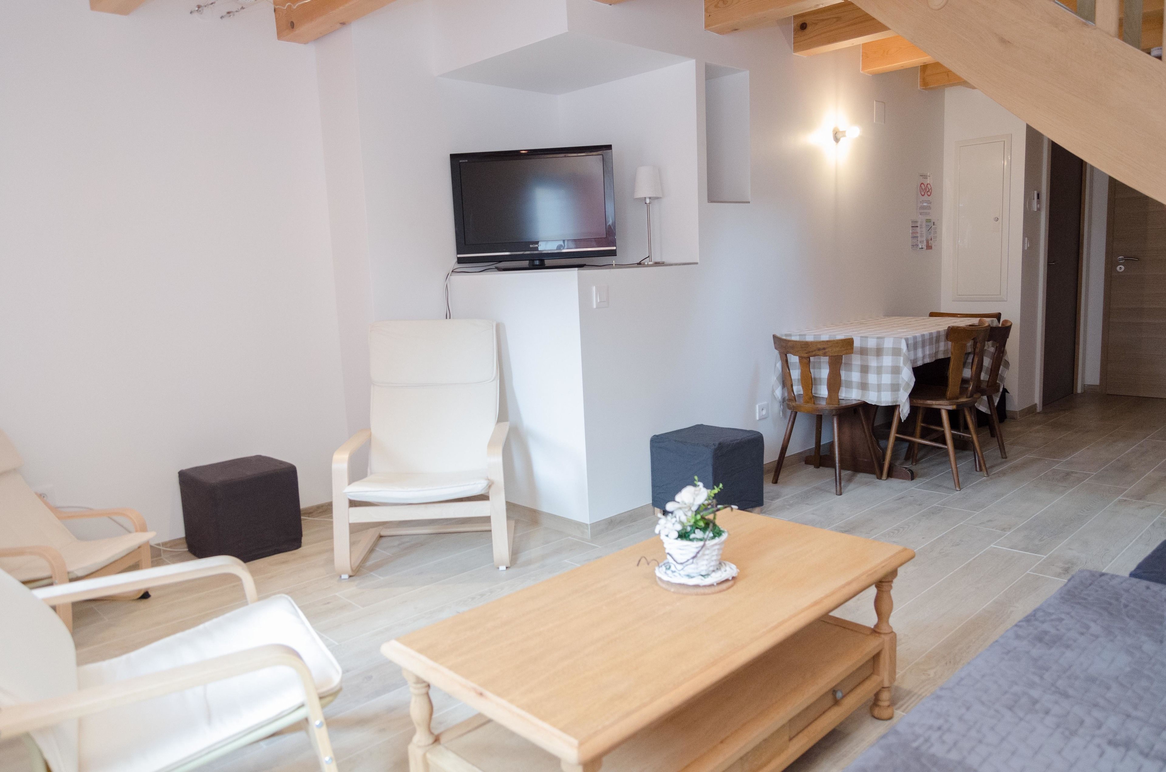 Una sala de estar moderna con una mesa de madera, sillas blancas, un televisor montado en la pared y un comedor con mesa y sillas.