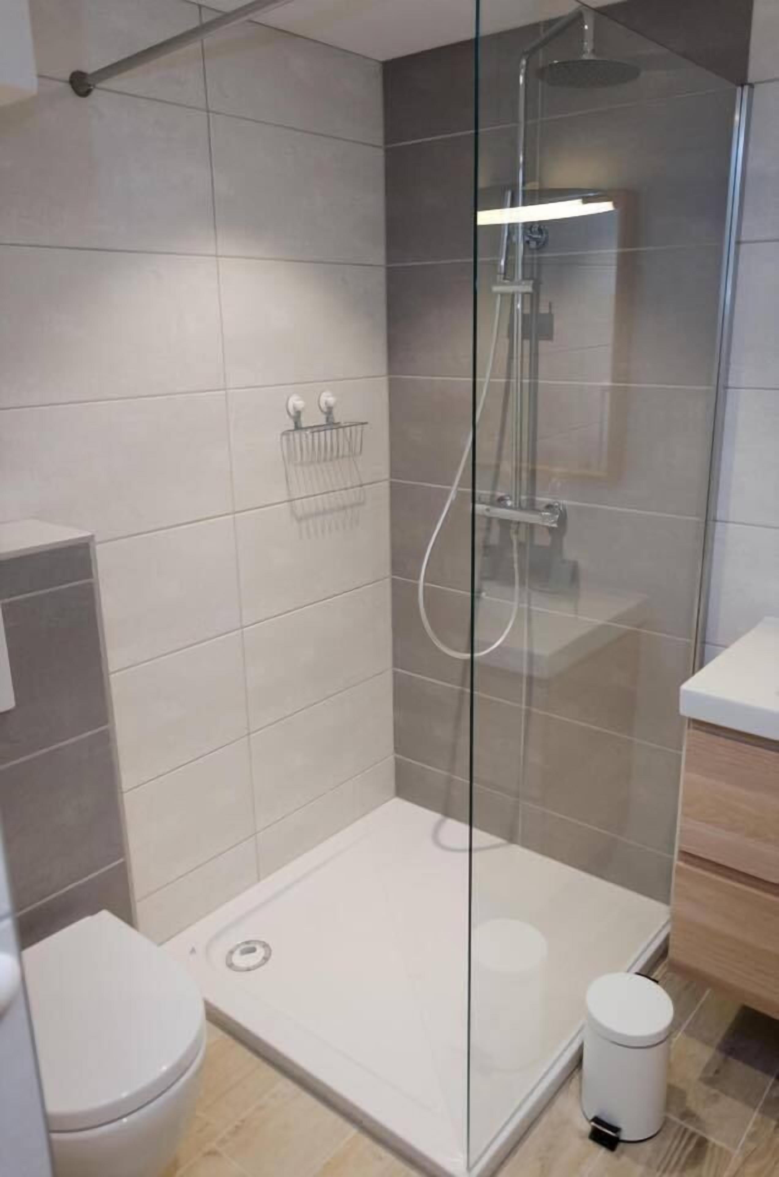 Un baño moderno con ducha envuelta en vidrio, inodoro blanco y un pequeño cubo de basura.