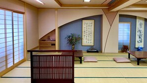 A traditional Japanese room with tatami flooring, a low wooden table, cushions, and calligraphy on the walls. - Kirishimaya Ryokan (Kusatsu)
