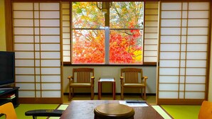 A traditional Japanese room with tatami flooring, a low table with a round container, two wooden chairs, and a window with autumn foliage. - Kirishimaya Ryokan (Kusatsu)