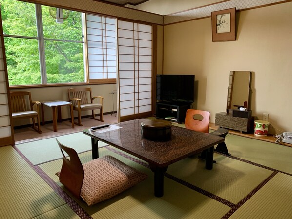 A traditional Japanese room with tatami flooring, a low table, two wooden chairs, a television, and a mirror. - Kirishimaya Ryokan (Kusatsu)