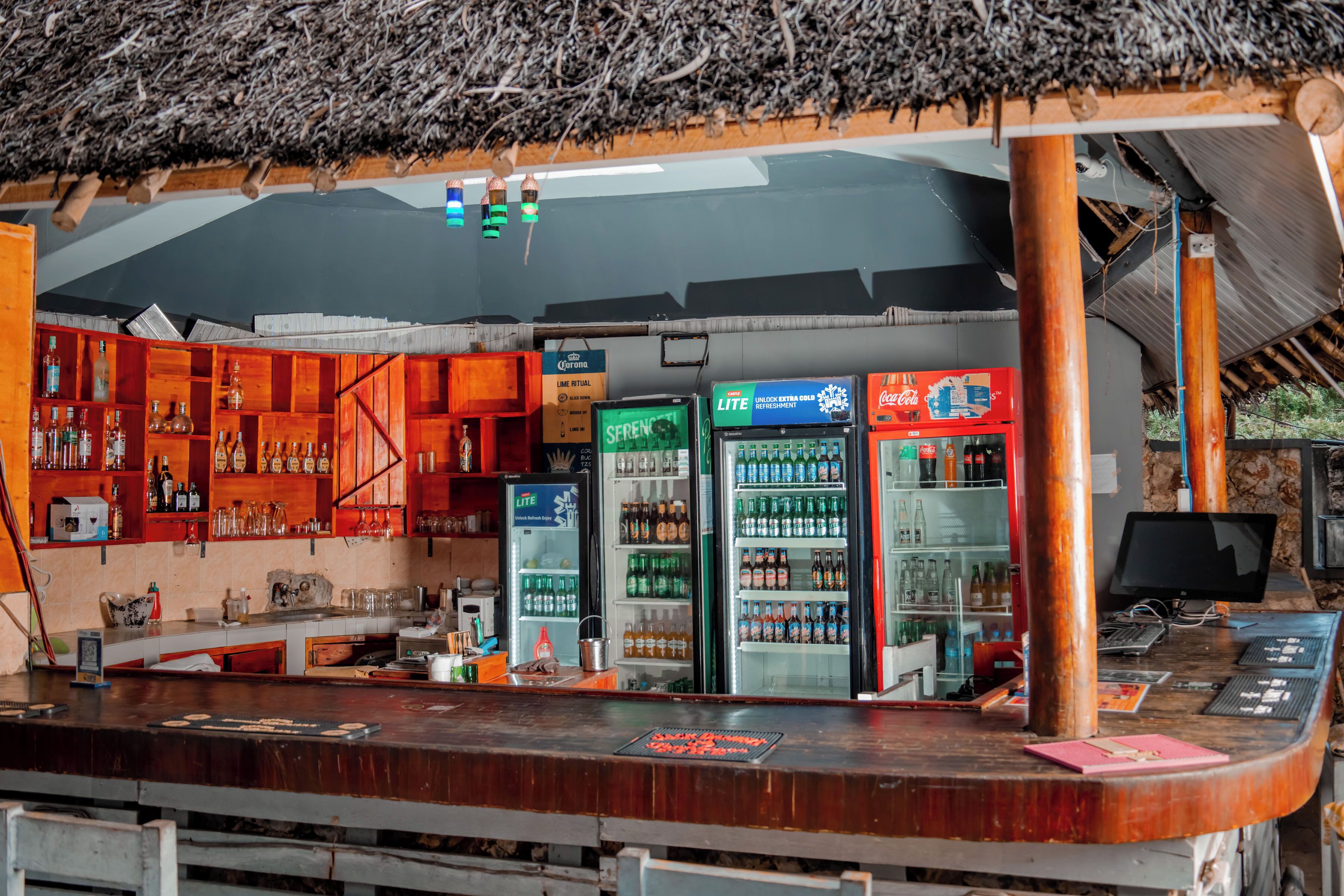 Un espace bar doté d’un toit de chaume, d’étagères remplies de bouteilles et d’un comptoir avec une caisse enregistreuse.