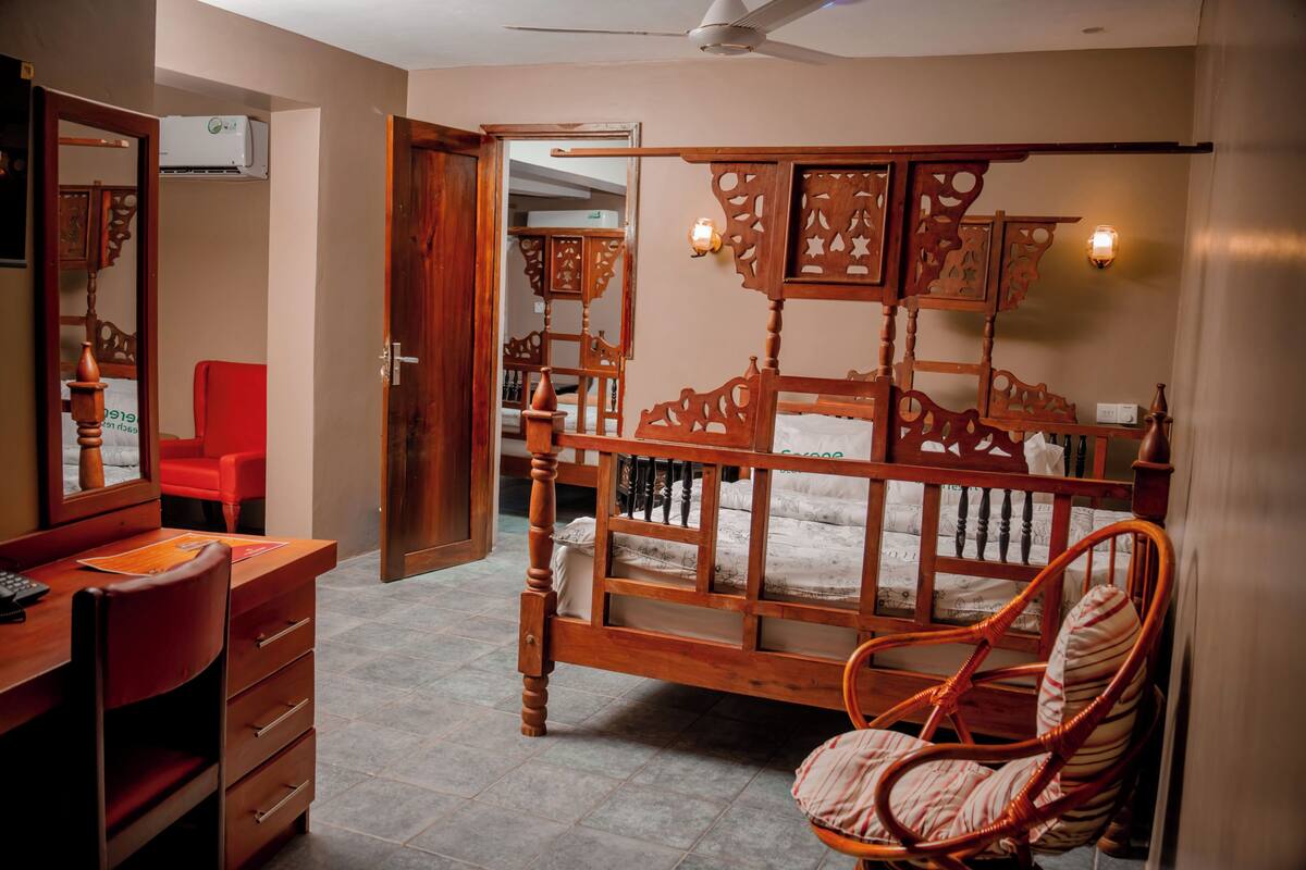 Un dormitorio con cama de madera, una silla roja, un escritorio con cajones y un espejo.