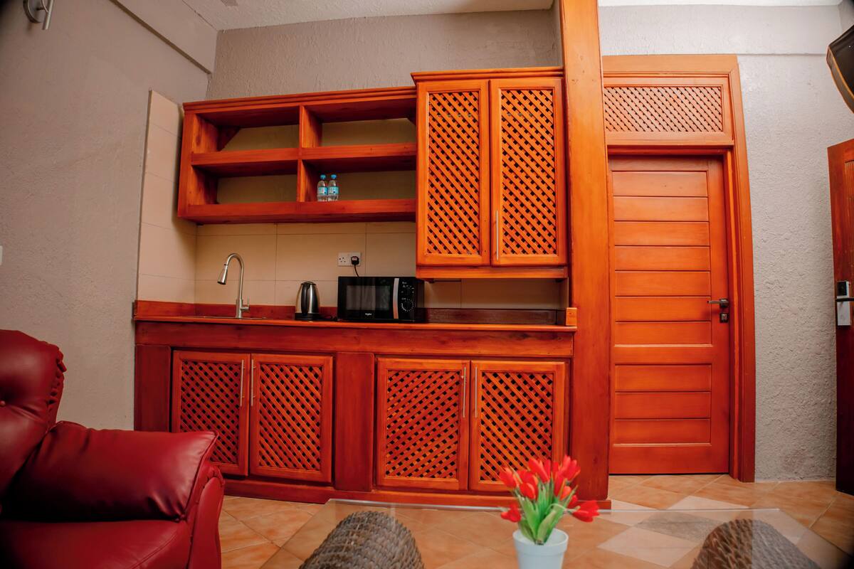 Un espacio habitable compacto con kitchenette, un sofá de cuero rojo y un mueble de madera con diseño de celosía.