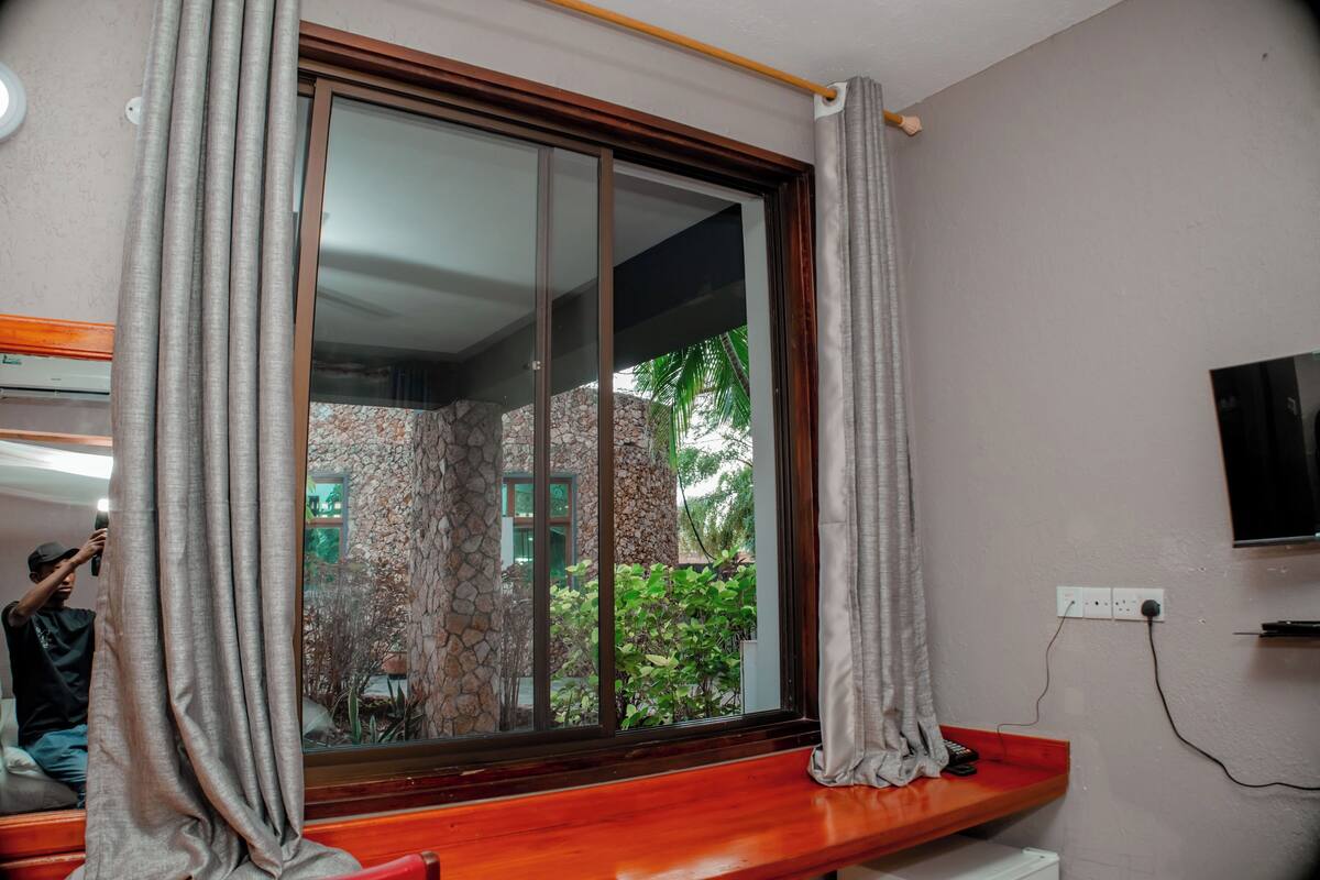Una habitación con un ventanal grande, un banco de madera, un televisor montado en la pared y un enchufe.