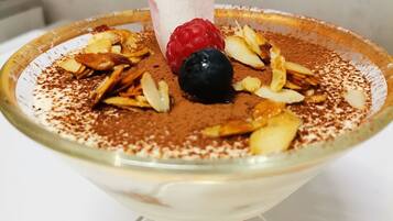 A dessert in a glass bowl with a raspberry, blueberry, and almond slices on top, dusted with cocoa powder.