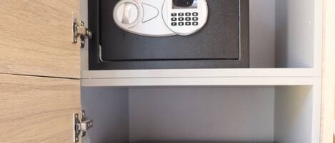 A black safe with a keypad and a small screen, placed on a shelf above a black refrigerator with the brand 'Oberazero' visible.