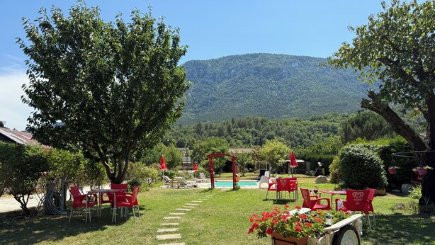 A garden with red chairs and tables, a pool, and a mountain in the background. - Rose des Pyrénées (Belvianes-et-Cavirac)