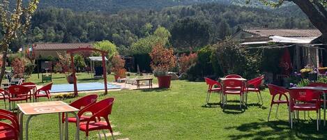 Uma área externa com assentos vermelhos, mesas, uma piscina pequena e vista para uma cordilheira.
