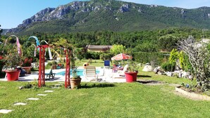 A pool area with lounge chairs and a red pergola, surrounded by potted plants and a mountainous backdrop. - Rose des Pyrénées (Belvianes-et-Cavirac)