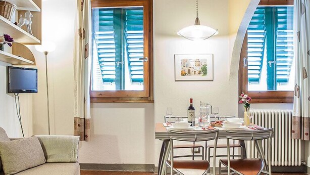 A cozy dining area with a wooden ceiling, a table set for two, and a television on a shelf. - San Lorenzo Apartment (Florence)