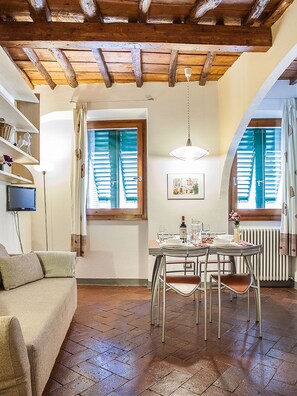 A cozy dining area with a wooden ceiling, a table set for two, and a window with shutters. - San Lorenzo Apartment (Florence)