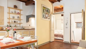 A compact kitchen with wooden shelves, a dining table set for two, and a bedroom with a bed and a door leading to another room. - San Lorenzo Apartment (Florence)