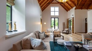 A spacious living room with a high wooden ceiling, a large window, and a cozy seating area with a sofa and chairs. - Taramea, family friendly home walking distance to Mora Wines (Lake Hayes)