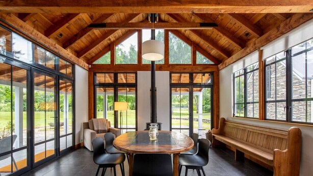A spacious room with a high ceiling, large windows, a round table with chairs, and a bench. - Taramea, family friendly home walking distance to Mora Wines (Lake Hayes)