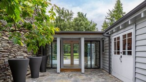 A stone-tiled patio with a wooden pergola and a door leading to a garage. - Taramea, family friendly home walking distance to Mora Wines (Lake Hayes)