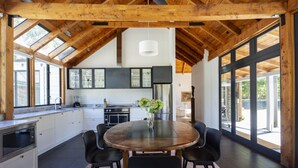 A modern kitchen with a wooden ceiling, large windows, and a central dining table with chairs. - Taramea, family friendly home walking distance to Mora Wines (Lake Hayes)