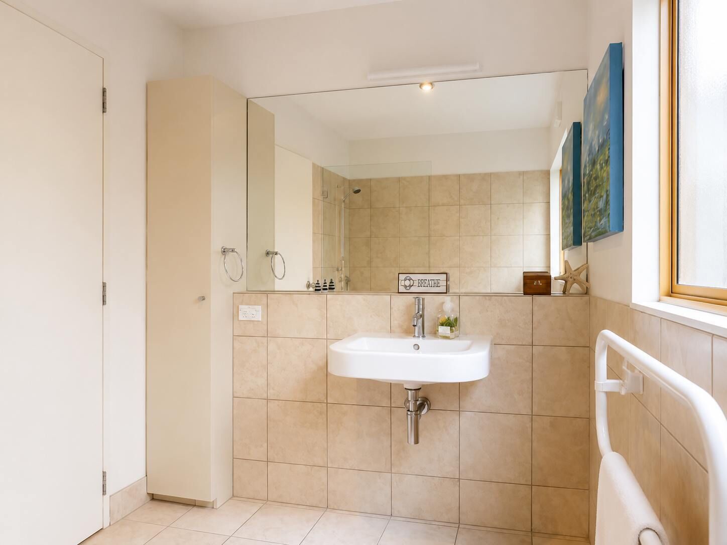 Ein Badezimmer mit Waschbecken, Spiegel und einem Schild mit der Aufschrift 'BREATHE'.