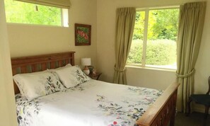 Uma cama com roupa de cama florida, cabeceira de madeira, mesa de cabeceira com abajur e uma cadeira.