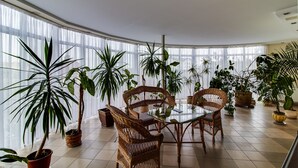 A dining area with wicker chairs and a glass table, surrounded by potted plants. - Hotel Galaktika (Lviv)