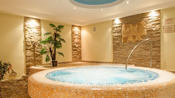 A hot tub with mosaic tiles, surrounded by stone walls and a potted plant. - Hotel Galaktika (Lviv)