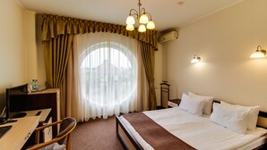 A hotel room with a bed, desk, chair, and a large window with curtains. - Hotel Galaktika (Lviv)