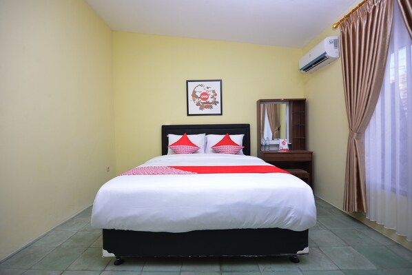 A hotel room with a bed, a framed picture on the wall, an air conditioning unit, a wooden nightstand, and a curtain. - Super OYO 1046 Omah Pathok (Yogyakarta)