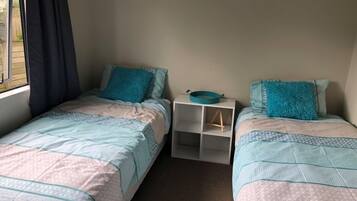 A small, cozy bedroom with two single beds, each with a teal pillow and a matching teal bowl on a white nightstand.