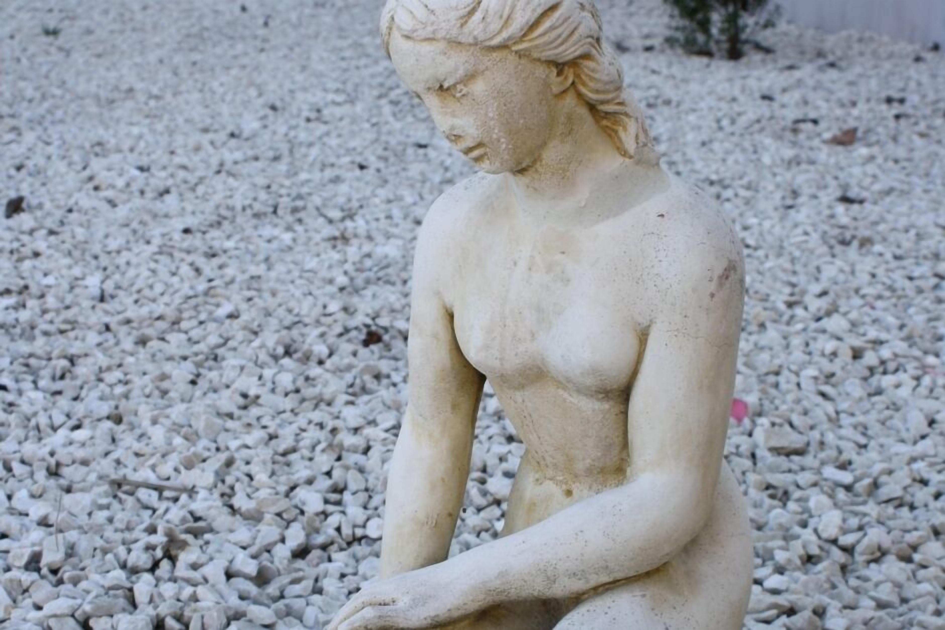 A statue of a seated woman on a gravel surface.