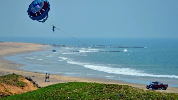 Une plage avec un pratiquant de parachute ascensionnel, une dune et un véhicule.