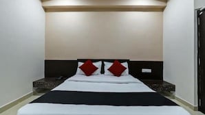 Une chambre d’hôtel avec un grand lit, une tête de lit agrémentée de deux oreillers rouges, une table de chevet et un panneau de commande fixé au mur.