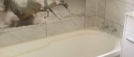 A bathroom with a bathtub, a tiled wall, and a white cabinet.