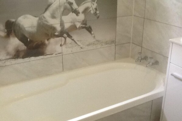 Ein Badezimmer mit Badewanne, gefliesten Wänden und einem weißen Schrank.