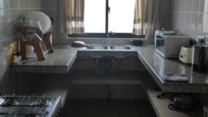 A kitchen with a gas stove, double sink, and a window with curtains. - Chez Odet (Mahé Island)
