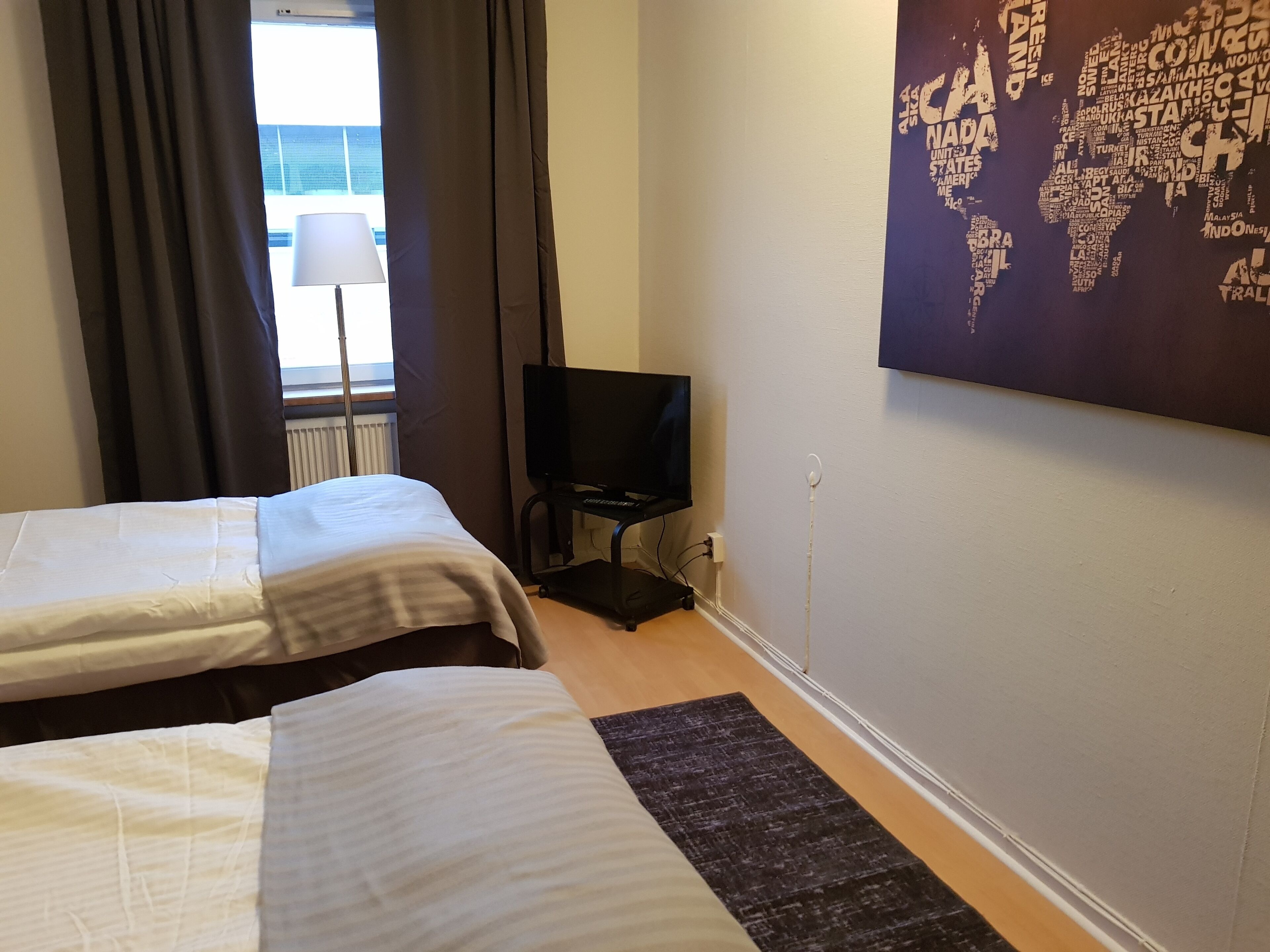 A hotel room with two beds, a TV, and a world map on the wall.