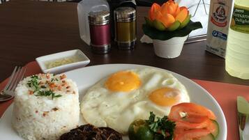 A plate of food including rice, eggs, vegetables, and meat, with condiments and a bottle of milk on the table.