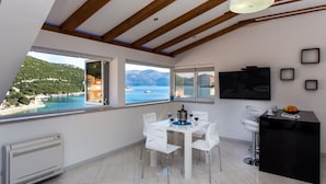 A modern kitchen with a dining area, large windows with a view of the sea, and a black countertop with a bowl of fruit. - Apartment Mali Skoj - Two-Bedroom Apartment with Sea View (Sudurad)